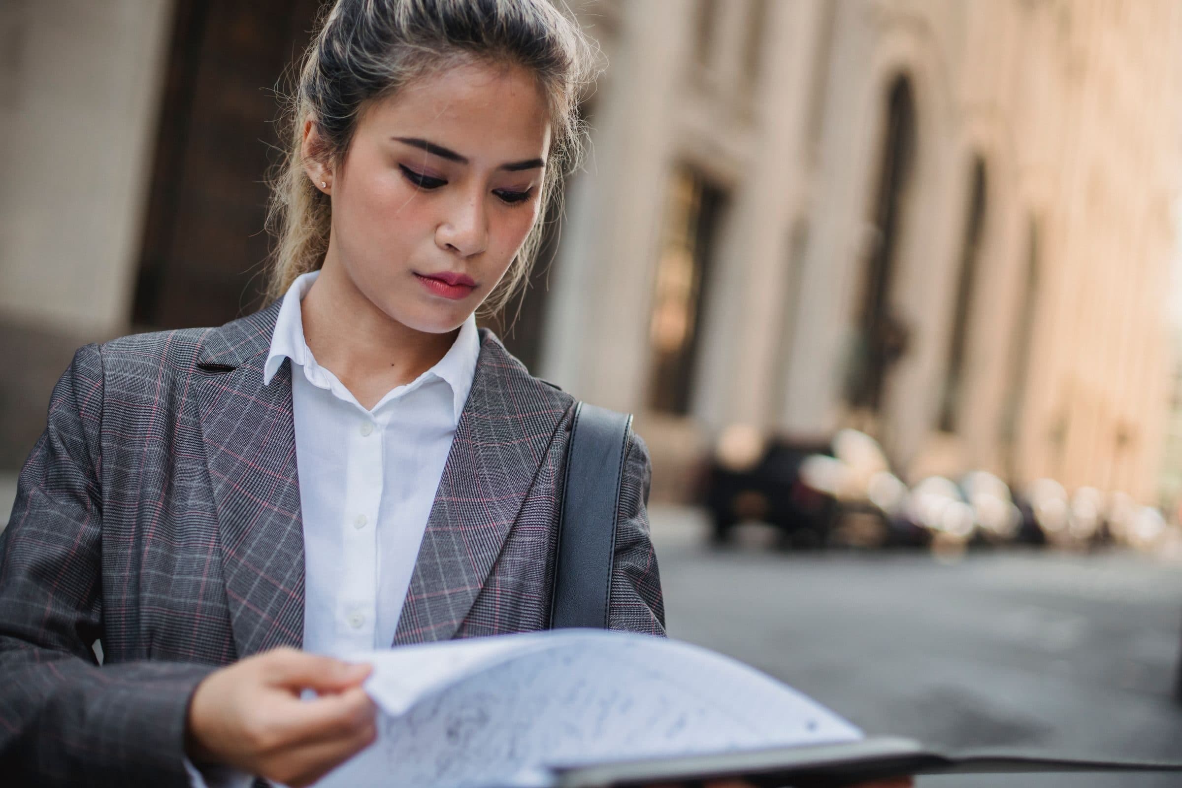 A young woman on a city street reviewing her printed documents
